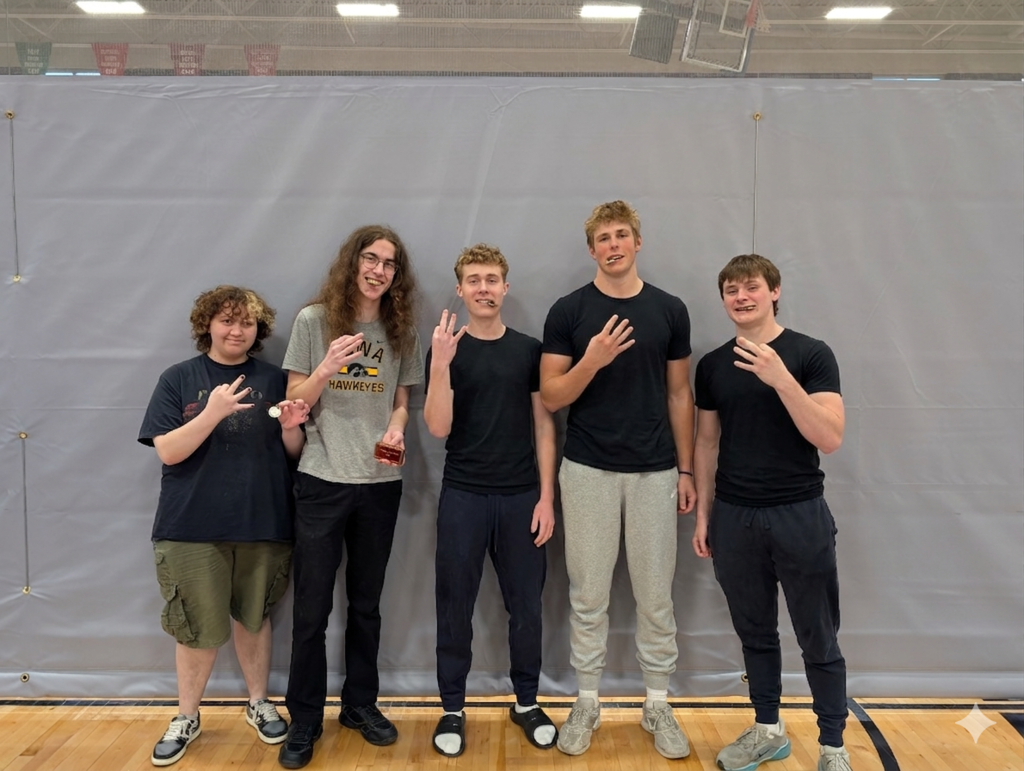 Five young students standing indoors on a gym floor, each holding up three fingers in a group pose against a gray backdrop.