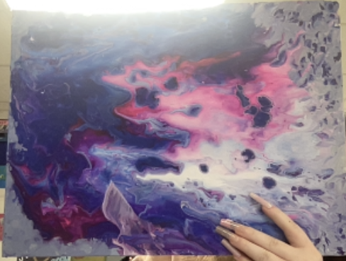 Abstract painting with swirling blue, pink, and purple tones, with a hand holding the canvas edge.