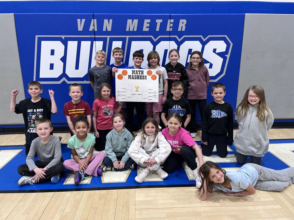 Group of elementary students posing in front of a Van Meter Bulldogs banner holding a Math Madness bracket poster in a gym.