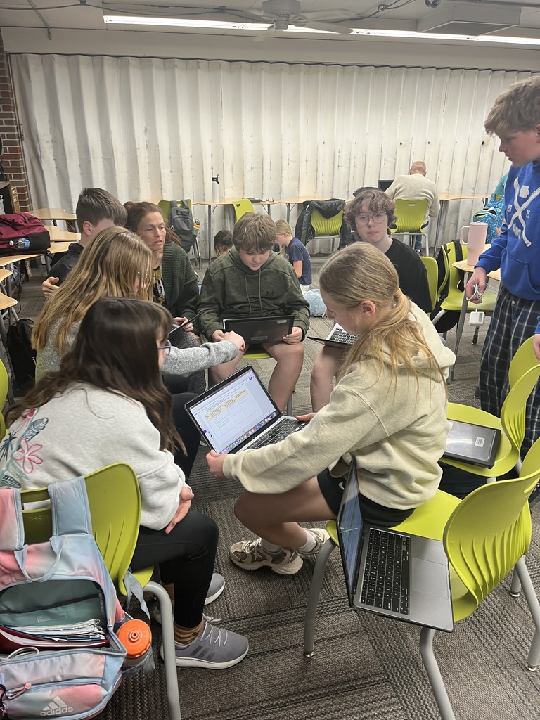 A group of students sitting in a classroom, collaborating and using laptops for a group project.