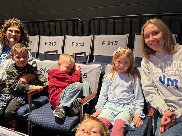 Children and two adults sit in theater seats, smiling casually, with kids relaxed and leaning into their chairs.