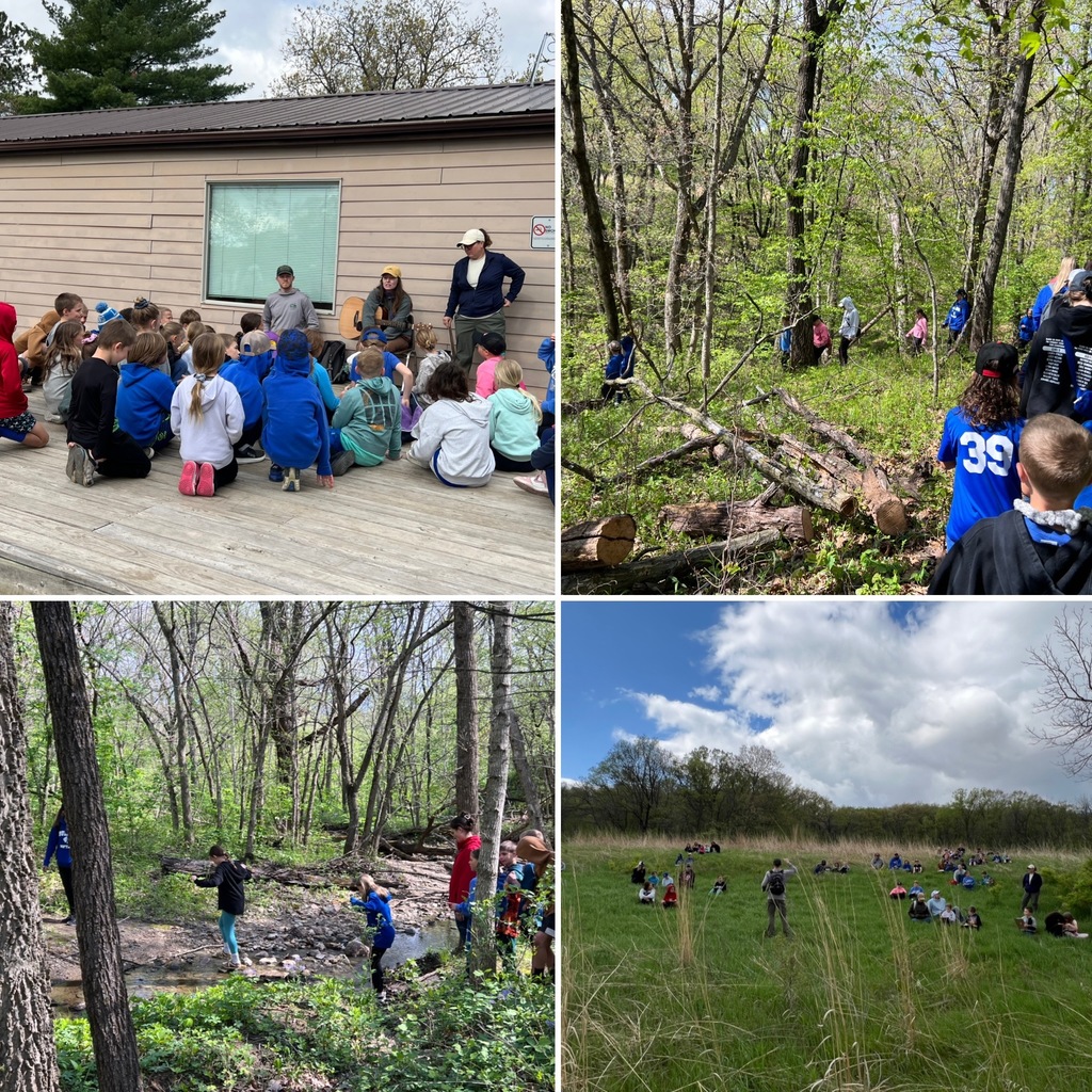 Children gathered outdoors listening to instructors near a wooden building on a sunny day.