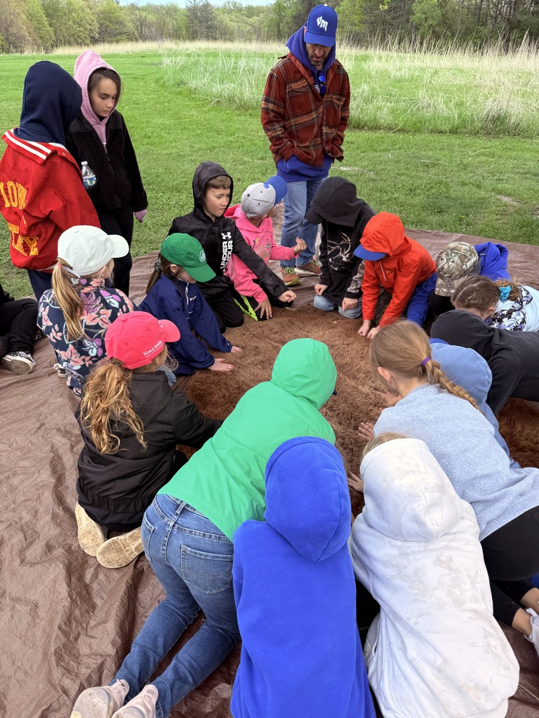 Children kneel around an animal hide on a tarp, touching the fur during a hands-on activity.