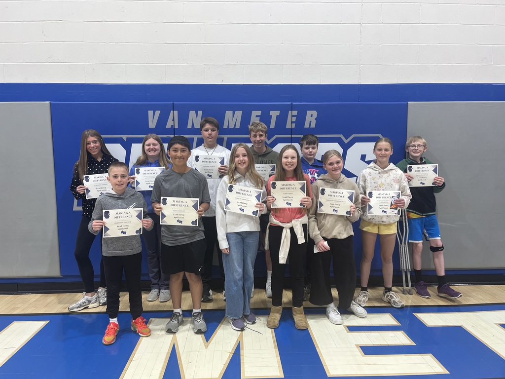 Students in a gym hold “Making a Difference” certificates before a blue Van Meter wall; one student uses crutches.