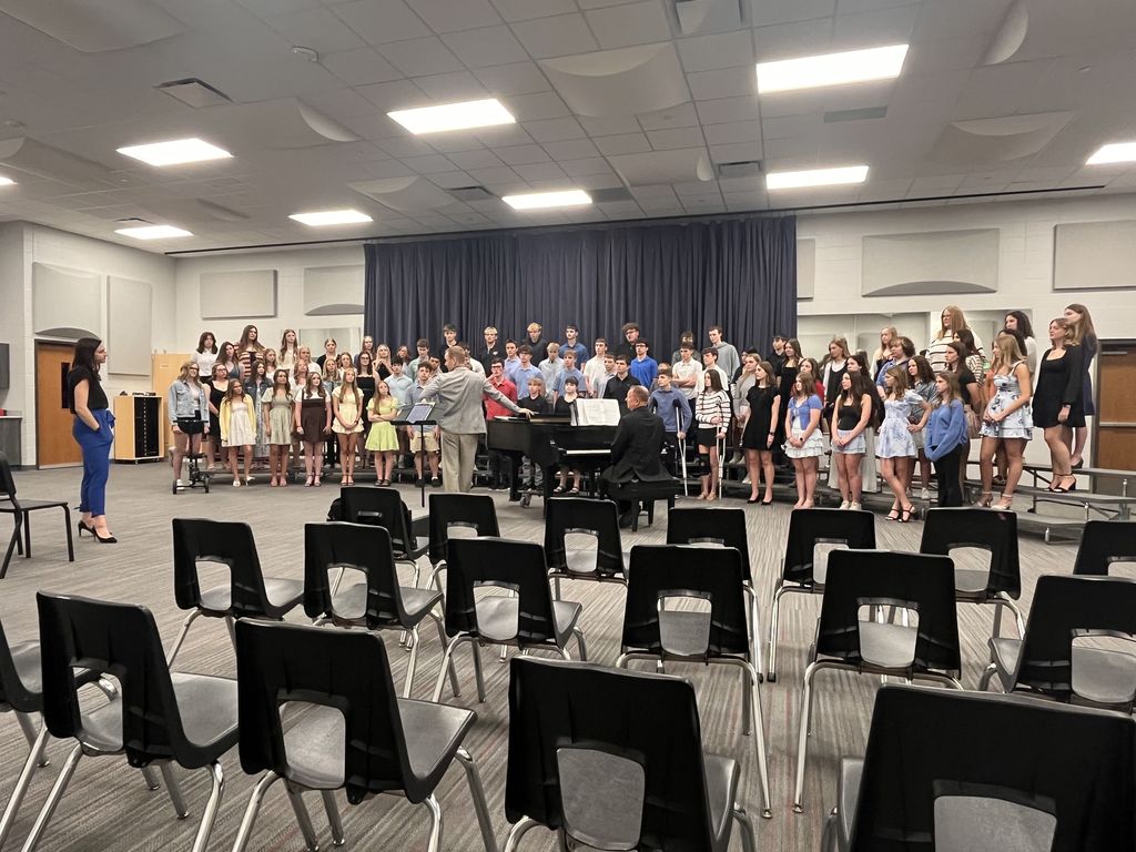 Large youth choir rehearsing in a spacious room with a conductor and pianist leading the group.