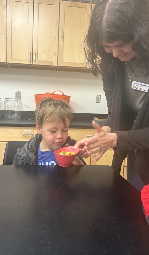 Teacher shows a young child a small bowl of dried flower petals during a hands-on classroom activity.