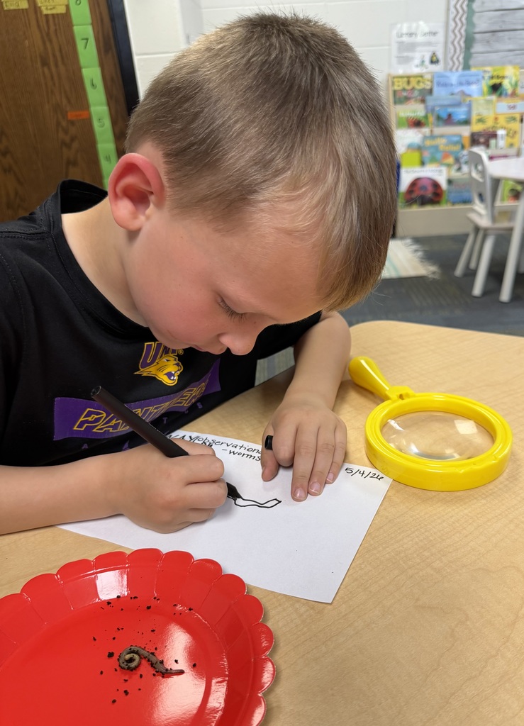 Young student carefully sketches a worm beside a magnifying glass and red plate holding the worm.