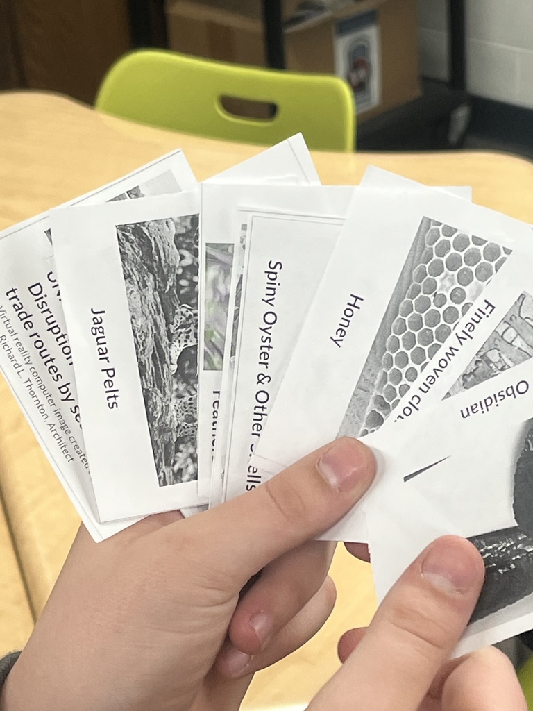 Student holds several printed cards with images and labels during a classroom trading activity.