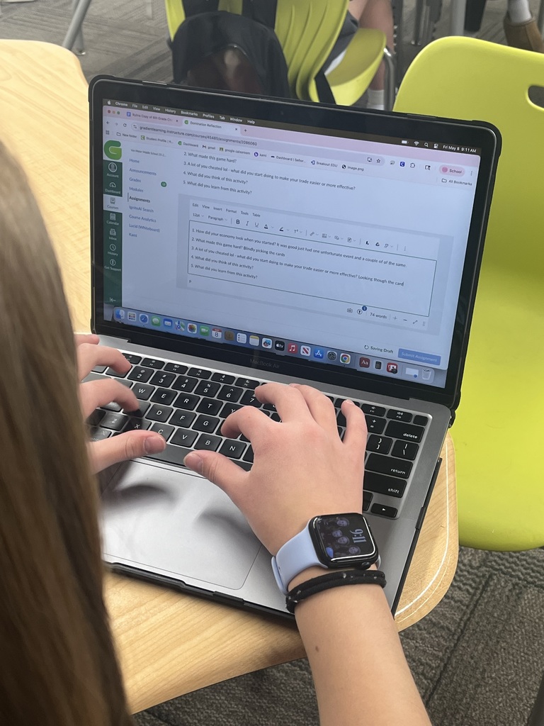 Student types reflections on a laptop after completing a classroom trading and economics activity.