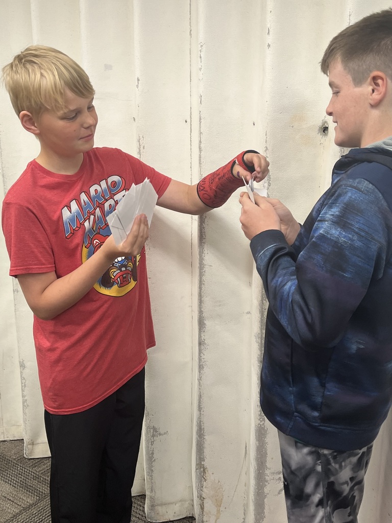 Two boys trade and examine printed cards during a classroom economics or trading simulation activity.