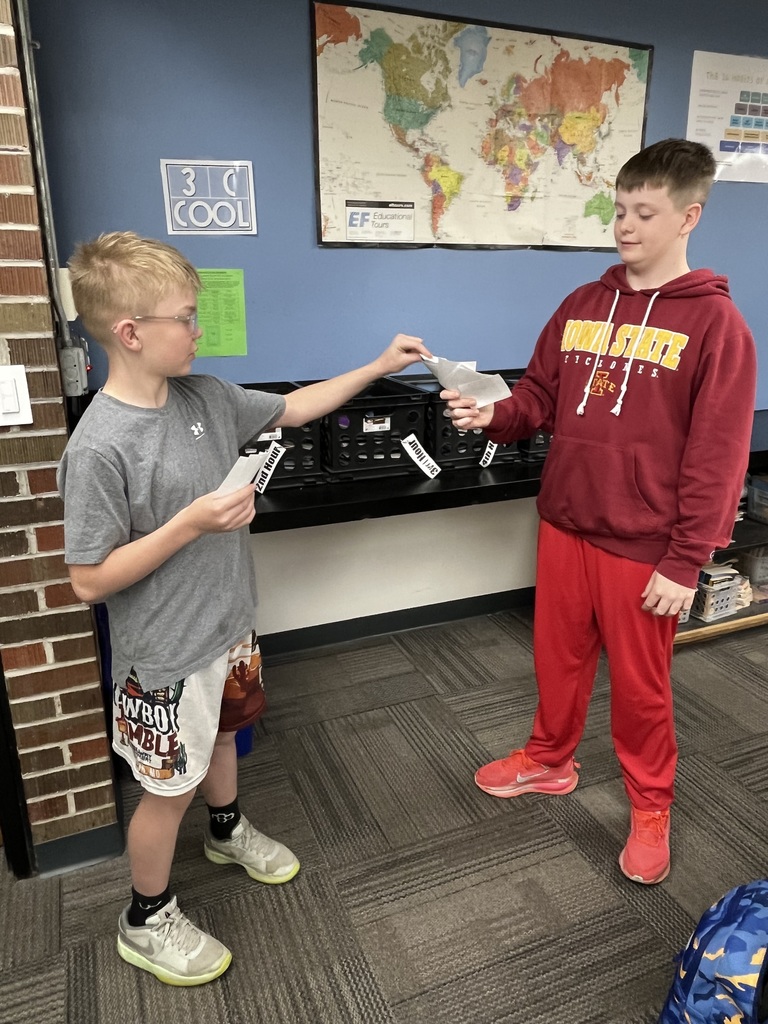 Two students exchange cards in a classroom while participating in a hands-on trading game.