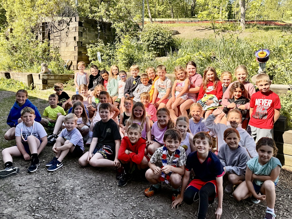 Group of children sitting outdoors on stone steps surrounded by greenery on a sunny day.