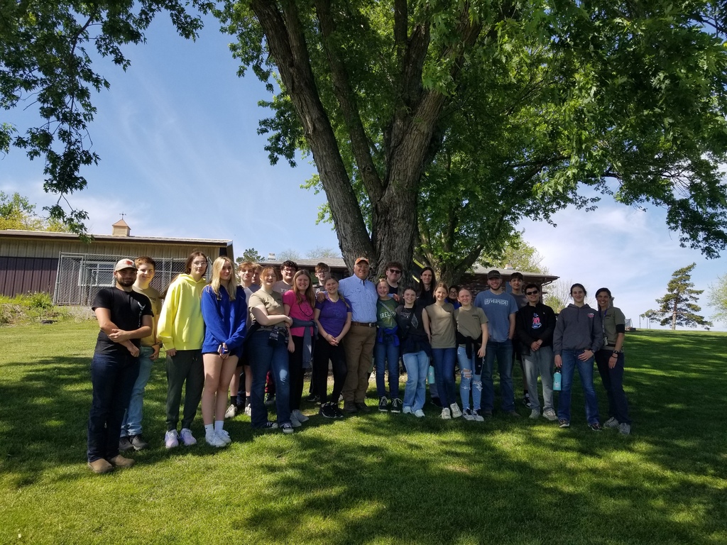 Large group of students and adults pose under a sprawling tree on a sunny spring day.