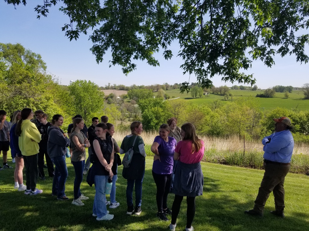 Group of students listens to a guide while standing on a grassy hill overlooking rolling countryside.