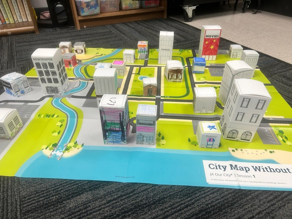 Student-built paper buildings arranged on a large city map mat during a Junior Achievement classroom activity.