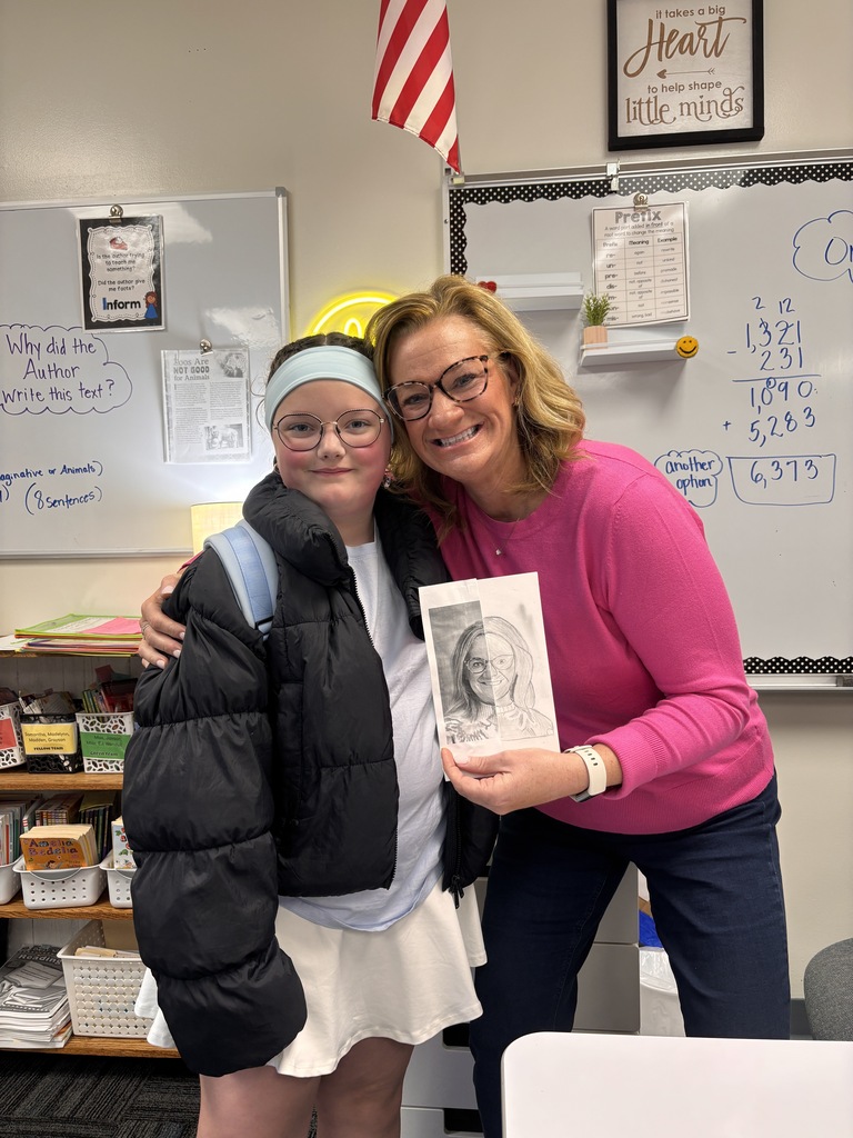Student and teacher smile in classroom while holding a detailed half-drawn portrait artwork.