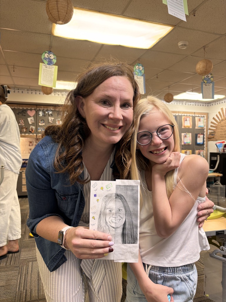 Teacher and smiling student hold a detailed portrait drawing together in classroom.