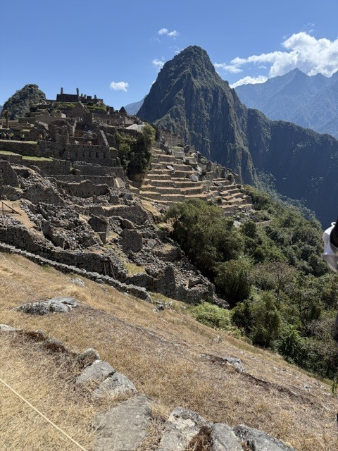 Ancient stone terraces and ruins of Machu Picchu with Huayna Picchu mountain towering in the background under a clear blue sky.