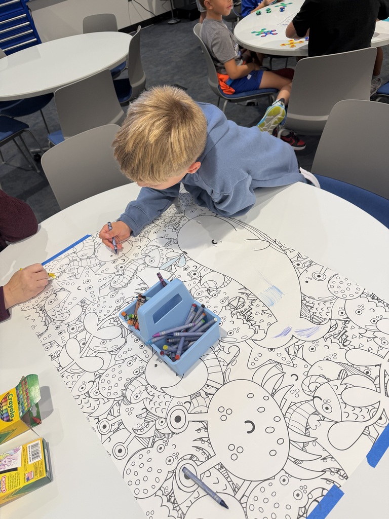 Child coloring a large, detailed underwater-themed poster with sea creatures using crayons at a round table in a classroom.