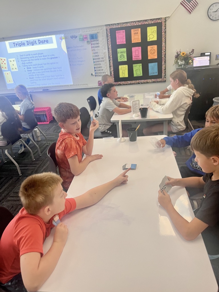 Students play “Triple Digit Dare” in small groups, using number cards to practice math at classroom tables.