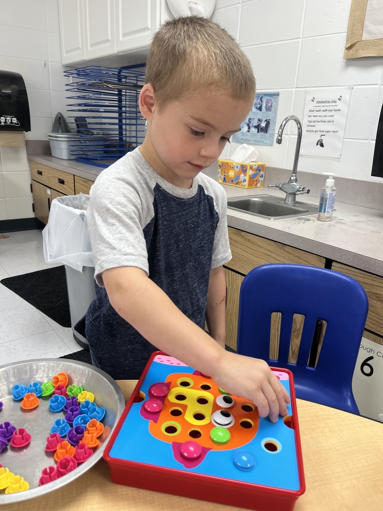 Young boy focused on placing colorful pegs into a ladybug-shaped pegboard at a classroom table.