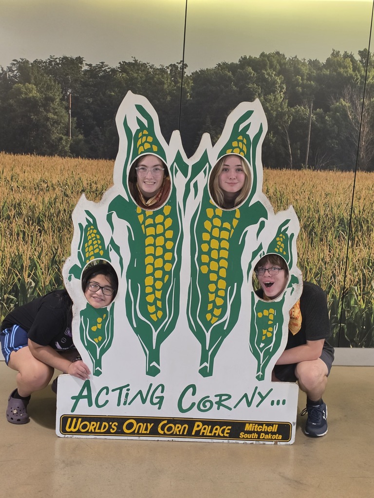 Four people posing behind a cutout board shaped like corn stalks with their faces showing, at the World's Only Corn Palace in Mitchell, South Dakota.