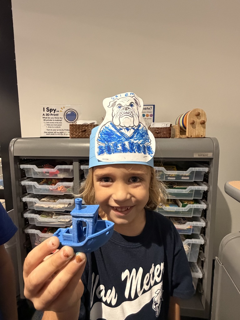 Child wearing a hand-colored bulldog paper crown smiles while holding a small blue 3D-printed boat model.
