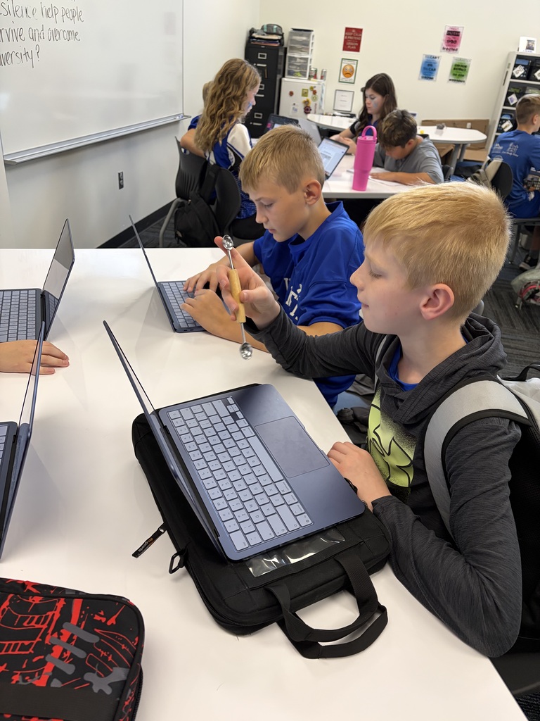 Two boys in a classroom using laptops and pencils, focused on their schoolwork at a white table.