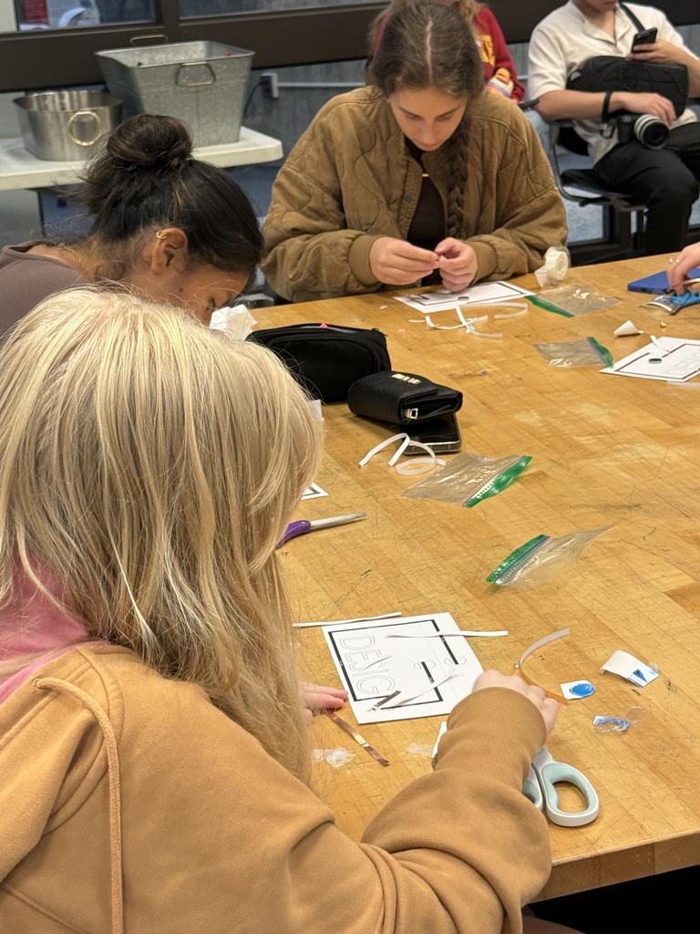 Students cut and assemble small materials over design worksheets during a hands-on classroom activity.