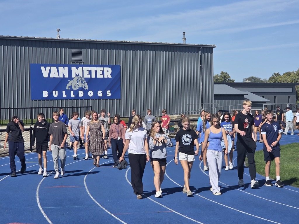Group of high school students walking on a blue running track outside Van Meter Bulldogs gym on a sunny day.