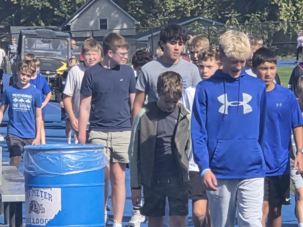 Group of boys walking outdoors near blue trash bins on a sunny day in a residential area.