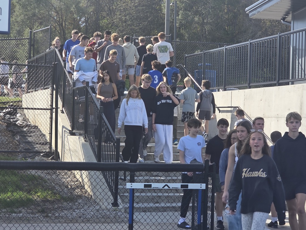 A diverse group of teenagers walking down outdoor stairs on a sunny day near a sports field.