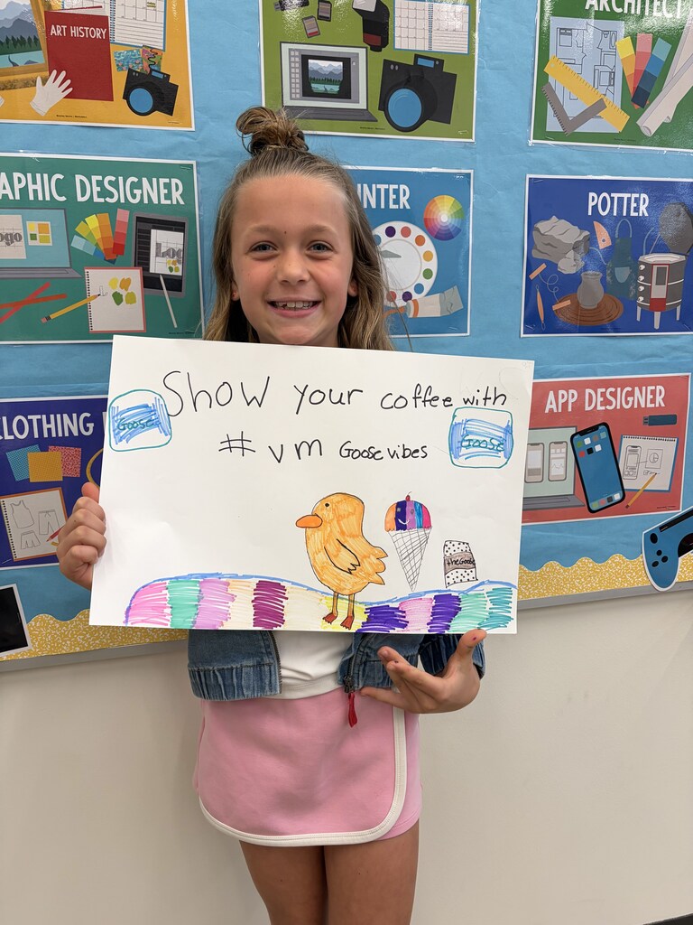 Young girl smiling and holding a colorful sign that says 'Show your coffee with #ym Good vibes' featuring a bird and coffee cup drawing.