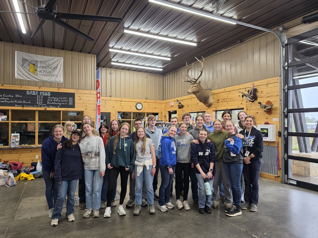 Group of young people posing inside a rustic lodge with wooden walls and mounted deer heads.