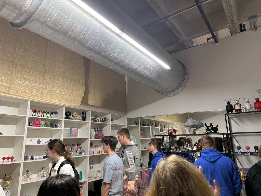 Students browse shelves filled with colorful figurines, sculptures, and collectibles in a contemporary art gallery.