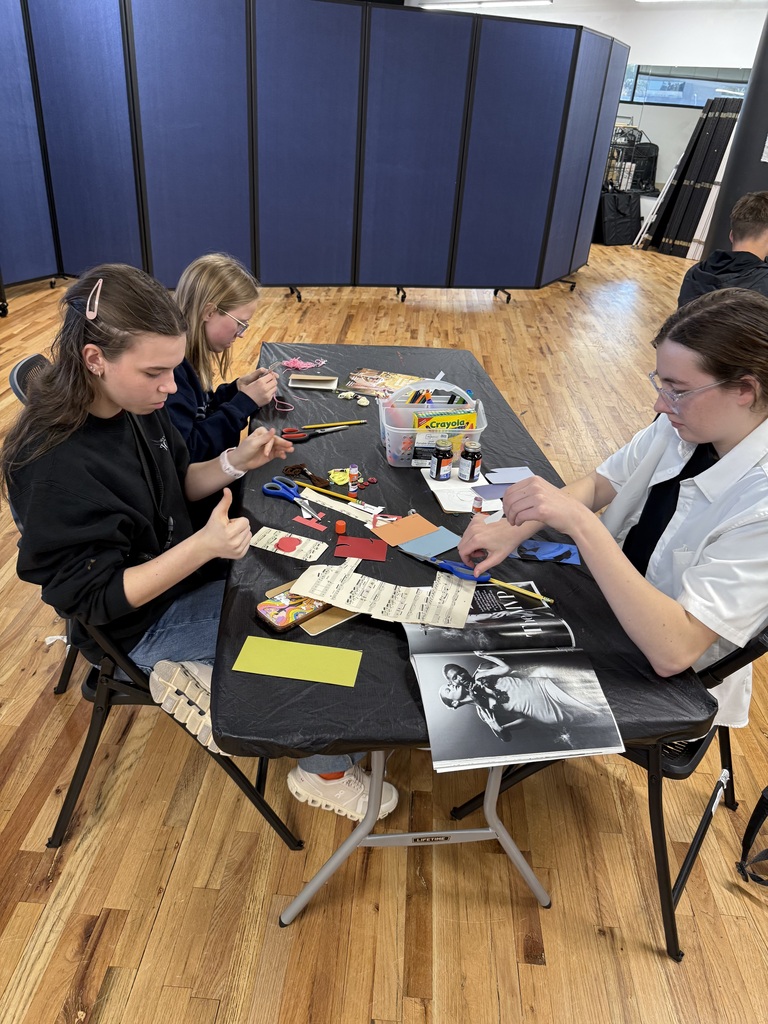 Three students concentrate on cutting and arranging paper, photographs, and other materials during a collage workshop.