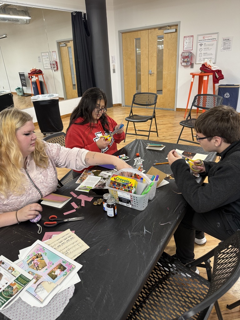 Three students work on paper collages using scissors, magazines, and colorful supplies at a shared art table.