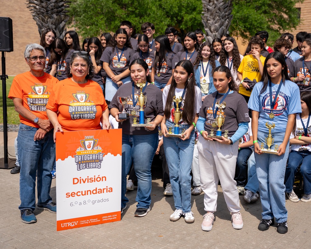 Group of students holding trophies stand in front of a sign that reads Division Secundaria.