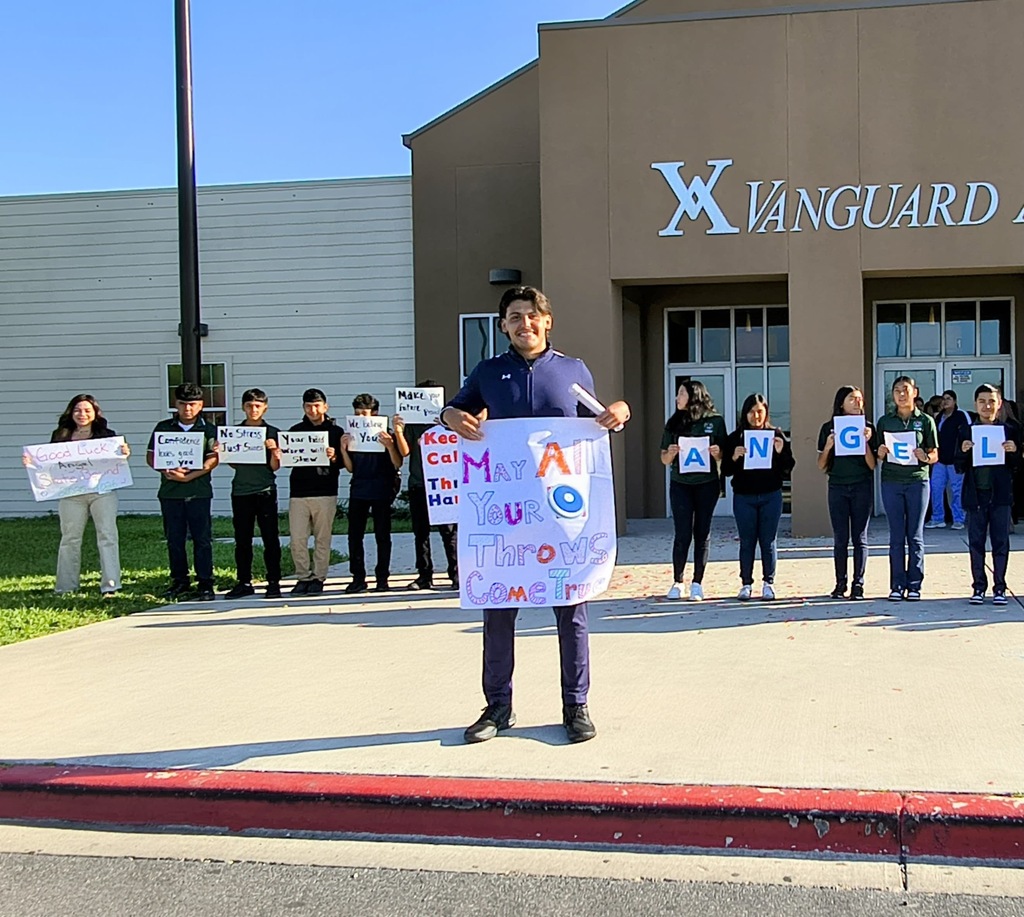 People holding signs in front of a building reading "X Vanguard" with a man in front holding a large sign.