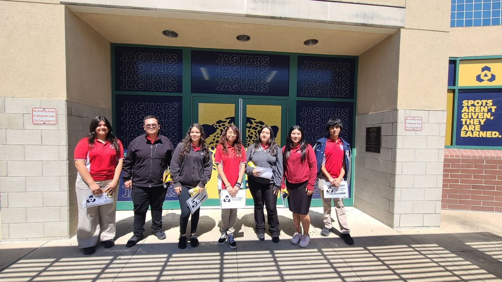 A group of people in matching red shirts stands outside a building with glass doors.