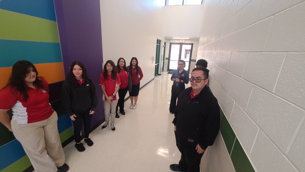 A group of individuals in red and black shirts stand in a brightly painted hallway with white walls and colorful stripes.