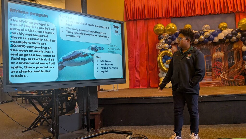 A person speaks in front of a screen with a large image of a penguin.