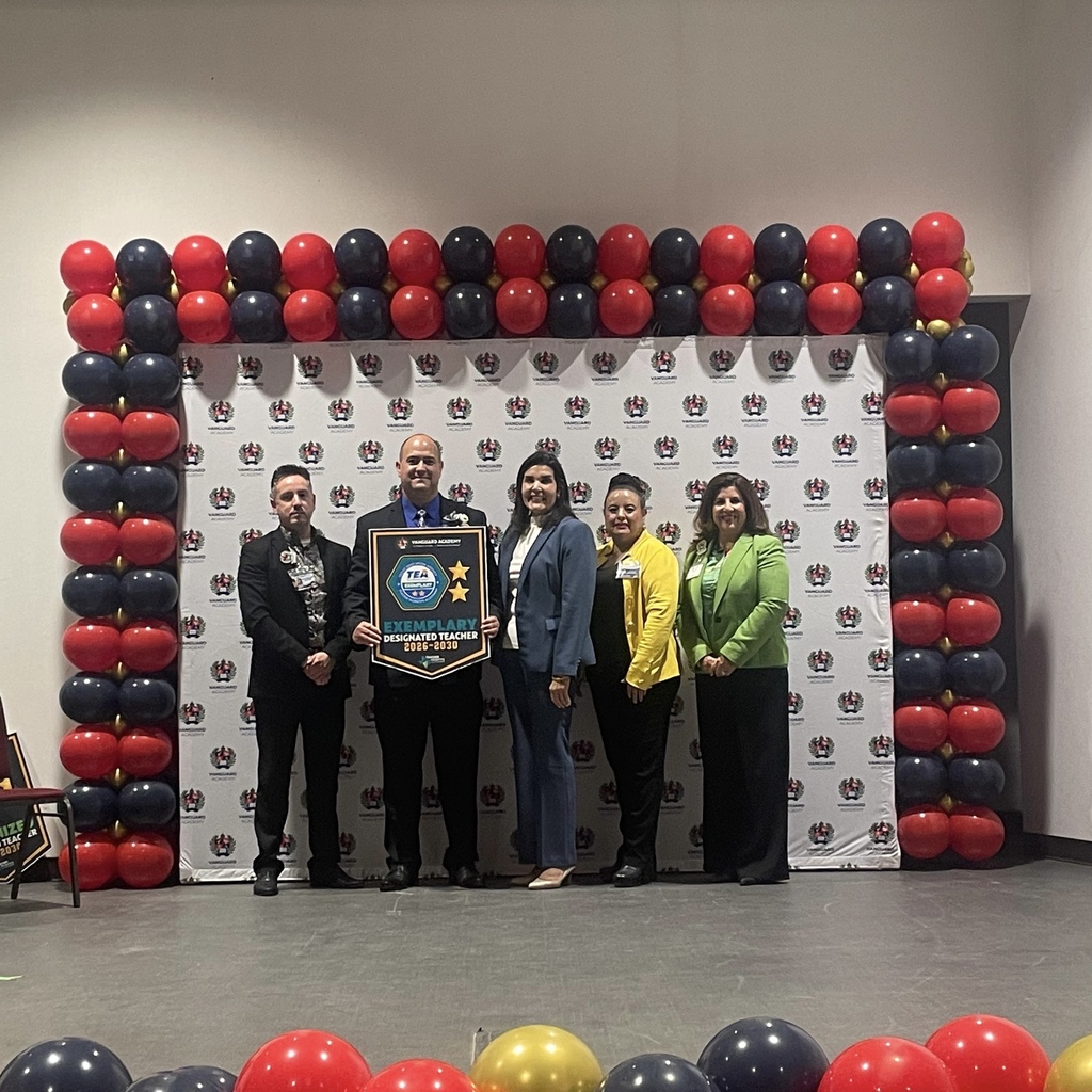 Five people stand on a stage in front of a wall of balloons. One person holds a plaque.