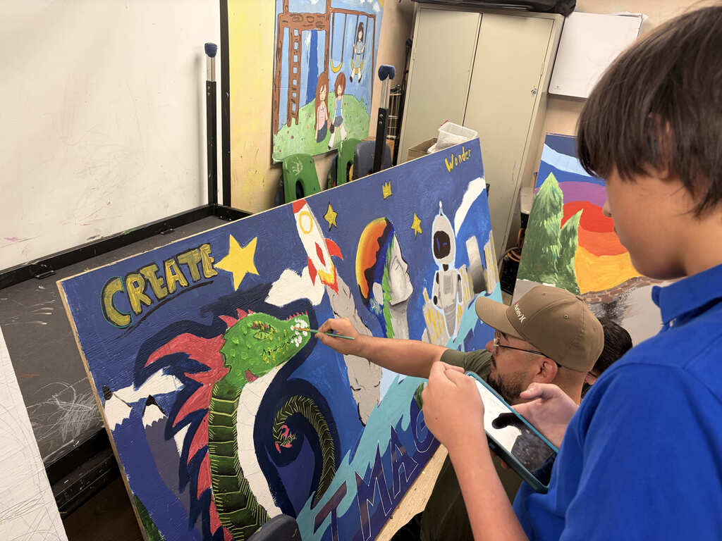 A boy in a blue shirt paints a mural with a dragon, stars, and space scenes.