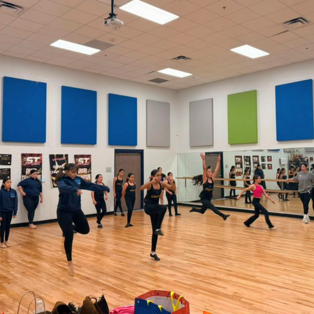 A dance studio with people performing various exercises. Some are leaping while others are standing.