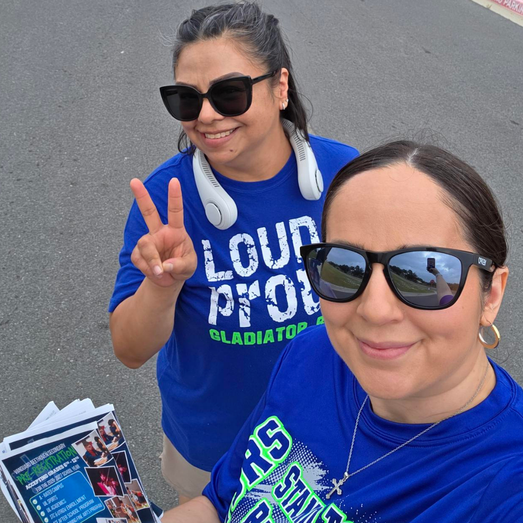 Two women in blue shirts with "LOUD PRO" printed on them. One is holding a paper, the other is smiling and making a peace sign.