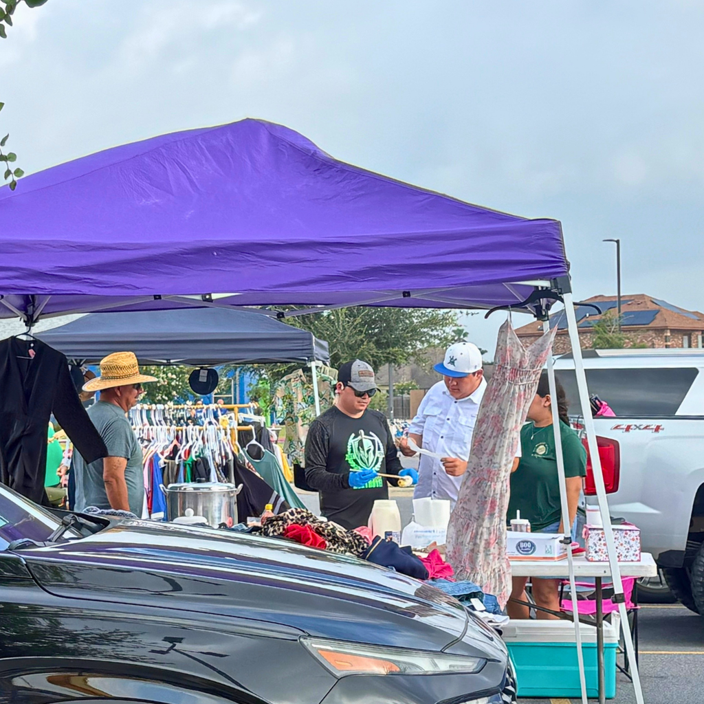 Several people are at an outdoor event. A purple tent stands over an open clothing sale.