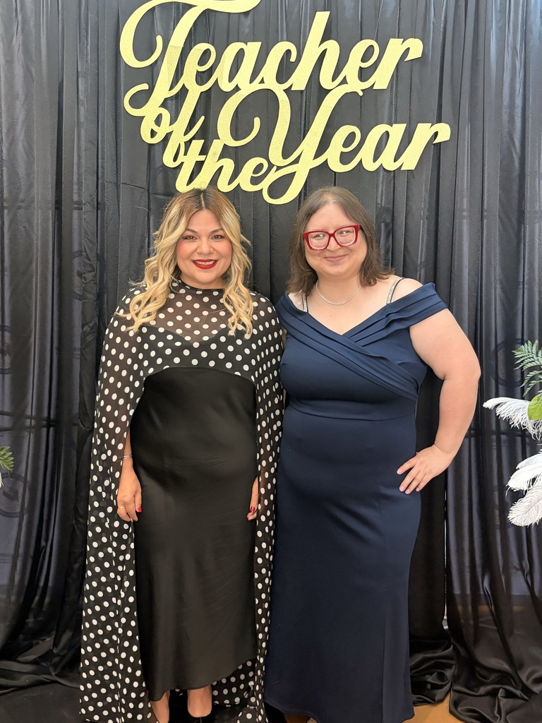 Two women stand next to each other in front of a black backdrop with yellow letters.