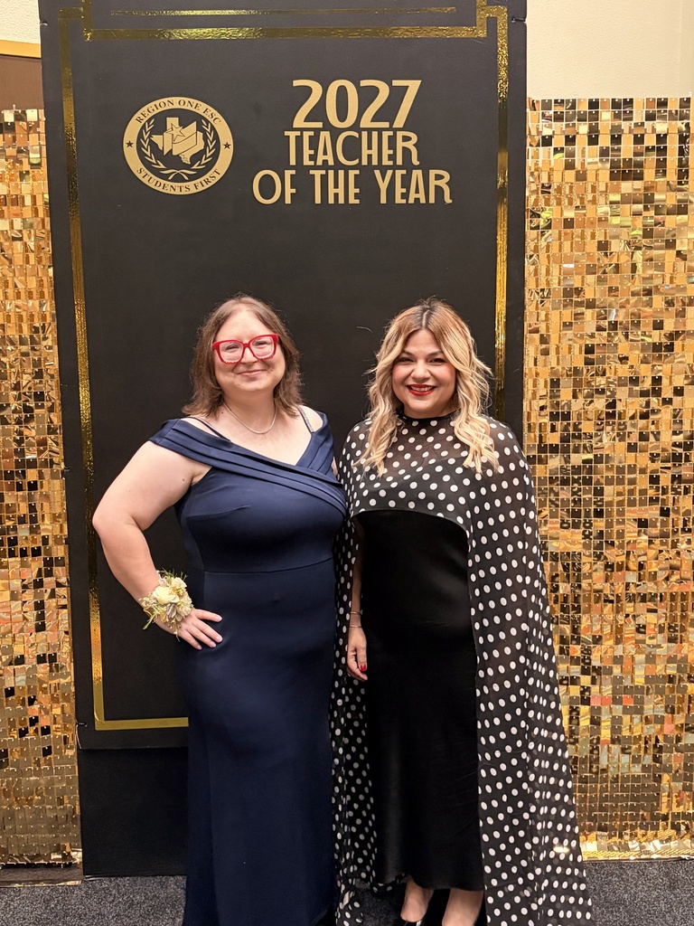 Two women in evening wear, standing in front of a sign for the 2027 Teacher of the Year.