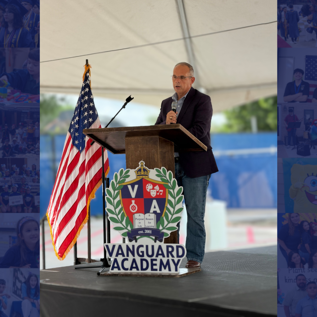 A man speaks at a podium, with an American flag behind him. The podium features the Vanguard Academy logo.